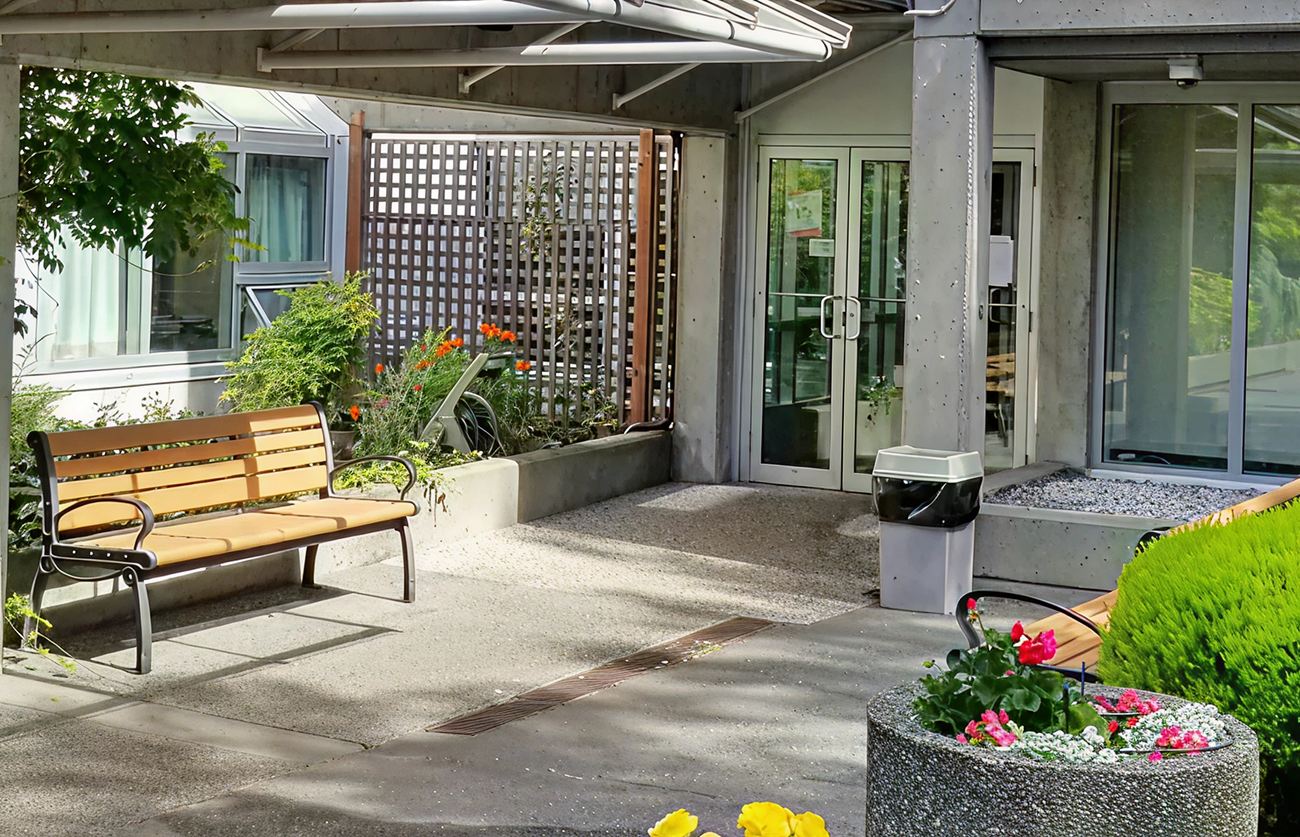 Exterior entrance of Sunset Lodge with a bench, walkway, and landscaped courtyard.