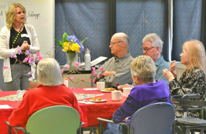 Residents seated around tables during a group activity at Sunset Lodge, with a staff member speaking to the group.